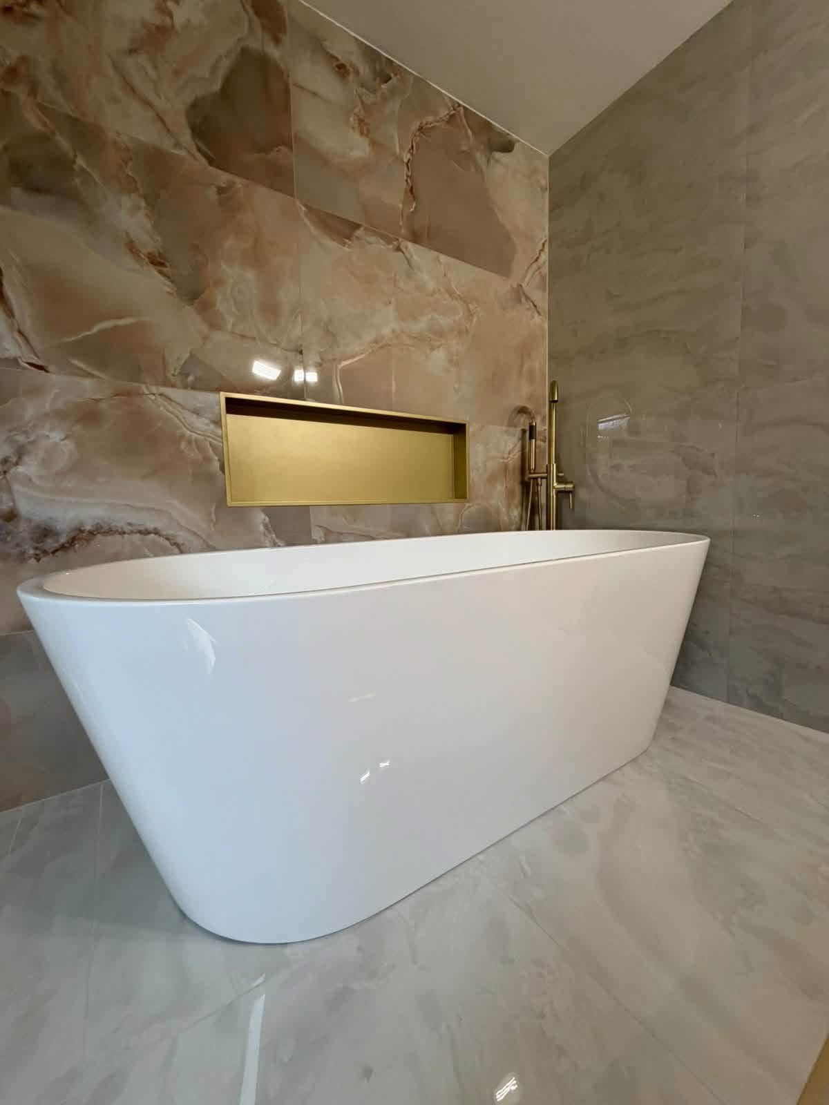 Freestanding bath with marble-effect tiles and gold niche